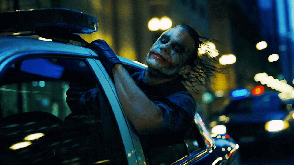 Heath Ledger in full Joker makeup with a somber expression on set.